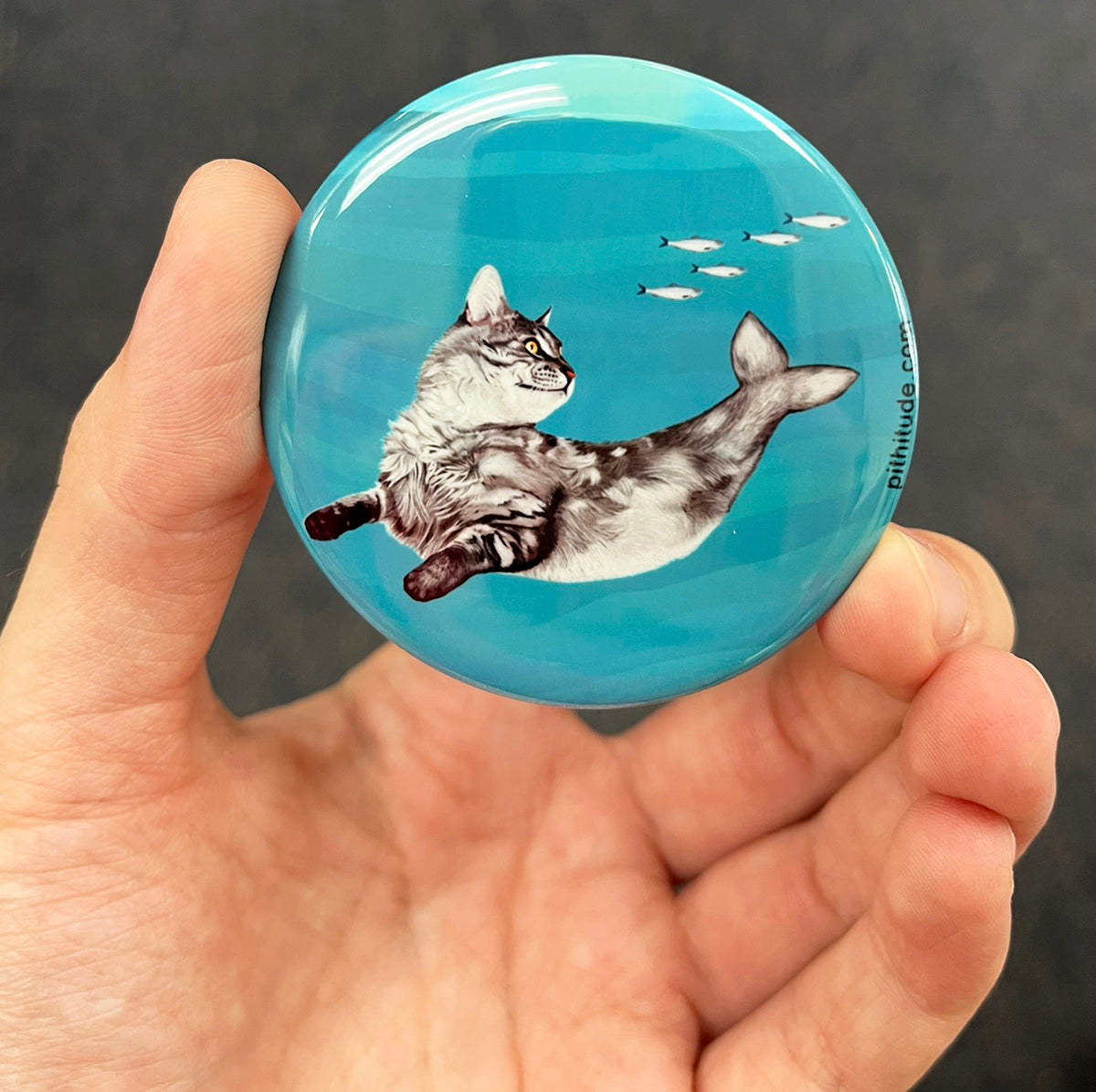 Whimsical cat mermaid magnet held in hand to show 2.25-inch size and glossy finish