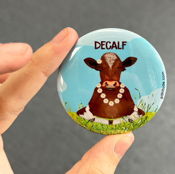Funny decaf cow magnet held in hand to show 2.25-inch size and glossy finish