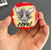 Funny feral cat magnet held in hand to show 2.25-inch size and glossy finish