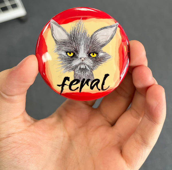 Funny feral cat magnet held in hand to show 2.25-inch size and glossy finish