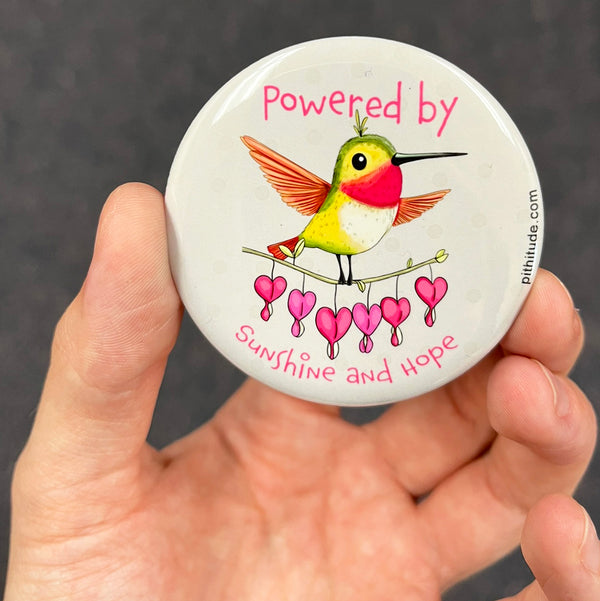 Inspirational hummingbird magnet held in hand to show 2.25-inch size and glossy finish