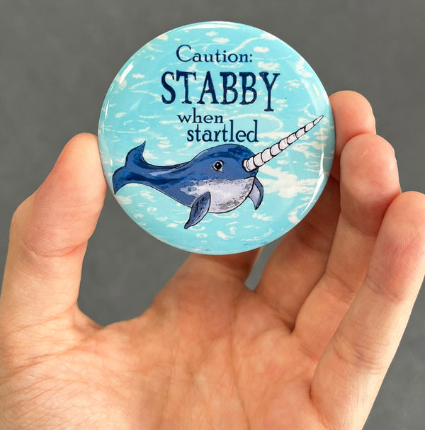 Funny narwhal magnet held in hand to show 2.25-inch size and glossy finish