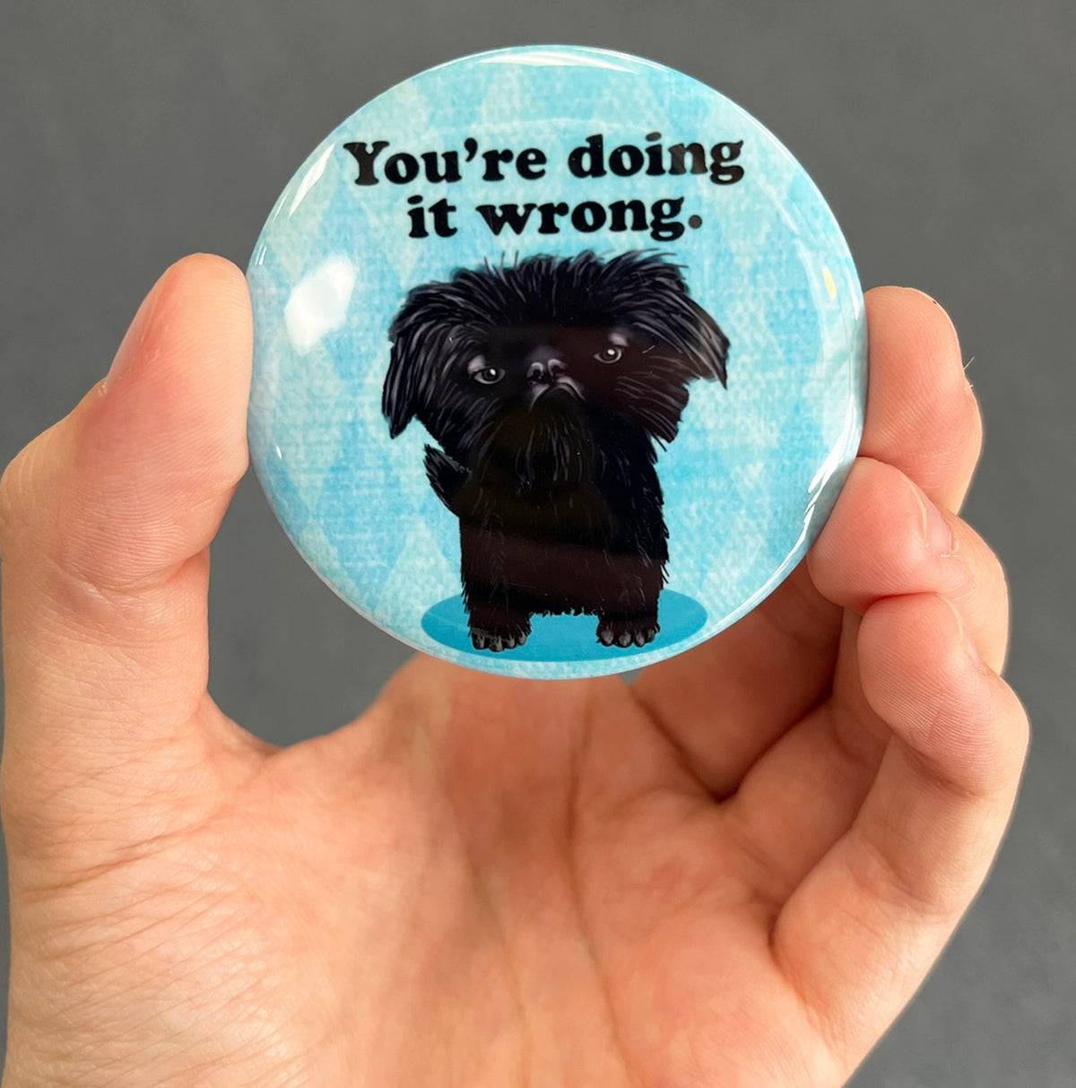 Funny dog magnet held in hand to show 2.25-inch size and glossy finish